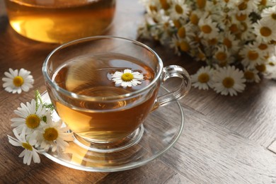 Photo of Aromatic tea in glass cup and chamomile flowers on wooden table, closeup