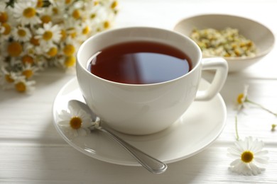 Photo of Aromatic tea in cup, chamomile flowers and spoon on white wooden table, closeup