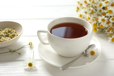 Photo of Aromatic tea in cup, chamomile flowers and spoon on white wooden table, closeup