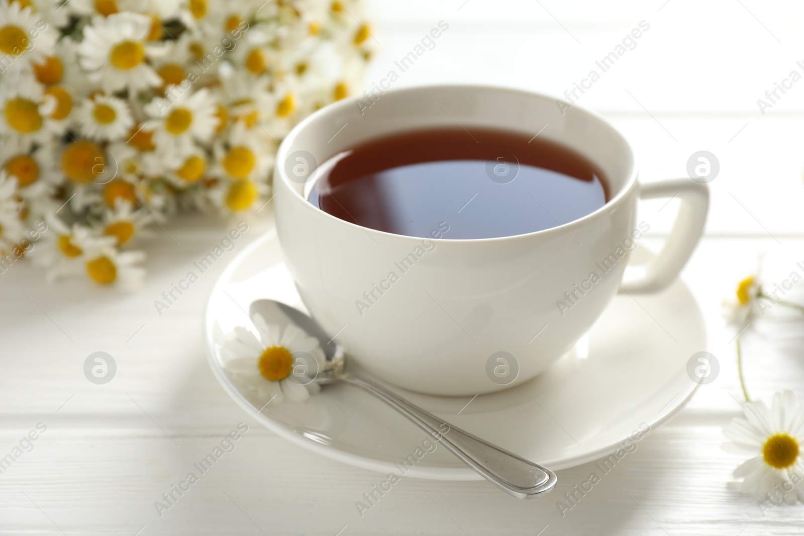 Photo of Aromatic tea in cup, chamomile flowers and spoon on white wooden table, closeup