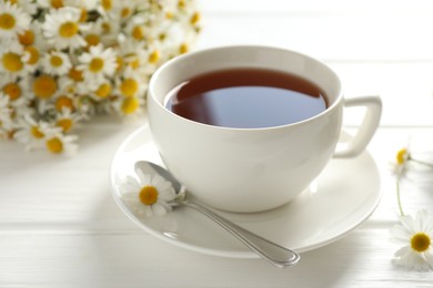 Photo of Aromatic tea in cup, chamomile flowers and spoon on white wooden table, closeup