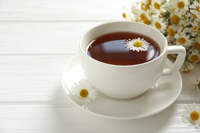 Photo of Aromatic tea in cup and chamomile flowers on white wooden table, closeup