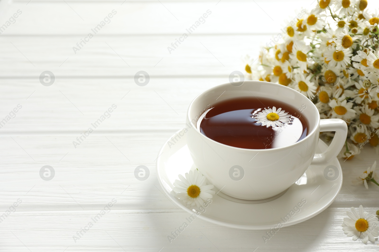 Aromatic tea in cup and chamomile flowers on white wooden table, closeup. Space for text Photo of Aromatic tea in cup and chamomile flowers on white wooden table, closeup. Space for text