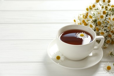 Photo of Aromatic tea in cup and chamomile flowers on white wooden table, closeup. Space for text