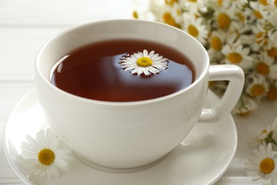 Photo of Aromatic tea in cup and chamomile flowers on white table, closeup