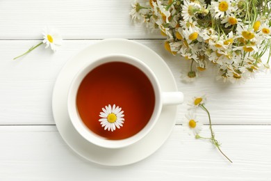 Photo of Aromatic tea in cup and chamomile flowers on white wooden table, flat lay
