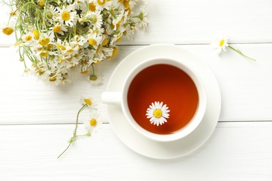 Photo of Aromatic tea in cup and chamomile flowers on white wooden table, flat lay