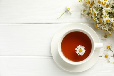 Photo of Aromatic tea in cup and chamomile flowers on white wooden table, flat lay. Space for text