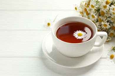 Photo of Aromatic tea in cup and chamomile flowers on white wooden table, closeup