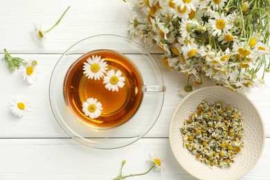 Photo of Aromatic tea in glass cup and chamomile flowers on white wooden table, flat lay