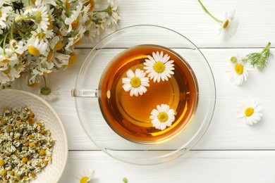 Photo of Aromatic tea in glass cup and chamomile flowers on white wooden table, flat lay