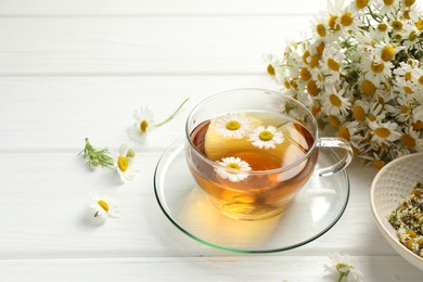 Photo of Aromatic tea in glass cup and chamomile flowers on white wooden table, closeup