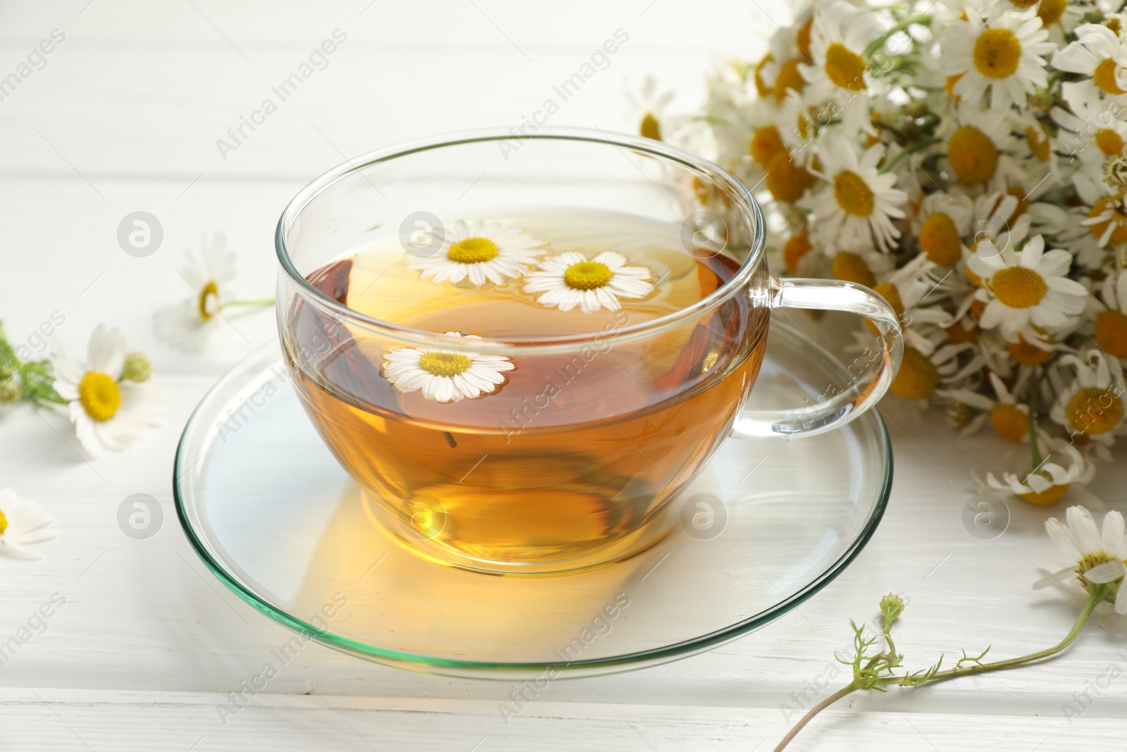 Aromatic tea in glass cup and chamomile flowers on white wooden table, closeup Photo of Aromatic tea in glass cup and chamomile flowers on white wooden table, closeup