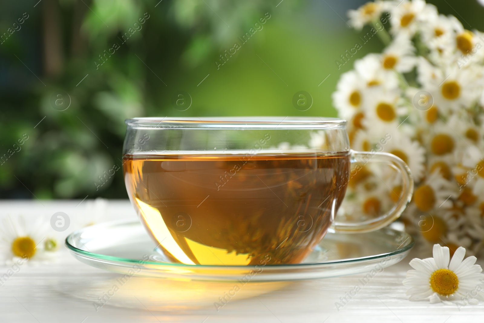 Photo of Aromatic tea in glass cup and chamomile flowers on white wooden table, closeup
