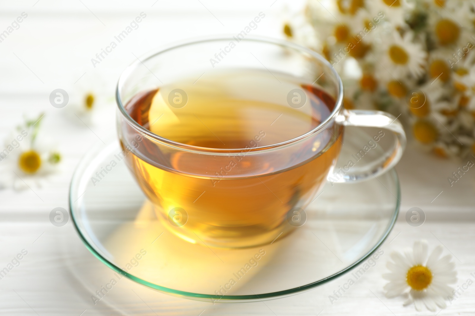 Aromatic tea in glass cup and chamomile flowers on white wooden table, closeup Photo of Aromatic tea in glass cup and chamomile flowers on white wooden table, closeup