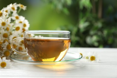 Photo of Aromatic tea in glass cup and chamomile flowers on white wooden table, closeup