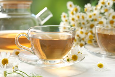 Photo of Aromatic tea in glass cups and chamomile flowers on white wooden table, closeup