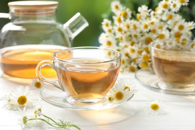 Photo of Aromatic tea in glass cups and chamomile flowers on white wooden table, closeup