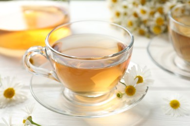 Photo of Aromatic tea in glass cups and chamomile flowers on white wooden table, closeup