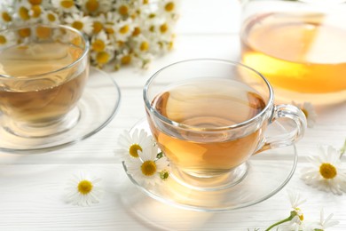Photo of Aromatic tea in glass cups and chamomile flowers on white wooden table, closeup