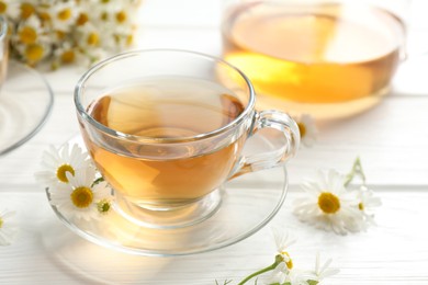 Photo of Aromatic tea in glass cups and chamomile flowers on white wooden table, closeup