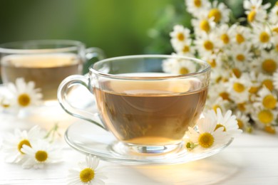 Photo of Aromatic tea in glass cups and chamomile flowers on white wooden table, closeup