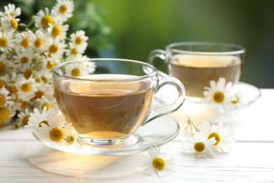 Photo of Aromatic tea in glass cups and chamomile flowers on white wooden table, closeup