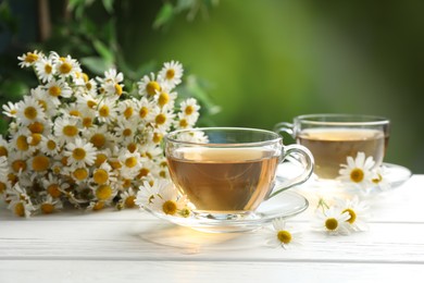 Photo of Aromatic tea in glass cups and chamomile flowers on white wooden table, closeup