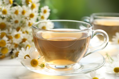 Photo of Aromatic tea in glass cups and chamomile flowers on white wooden table, closeup