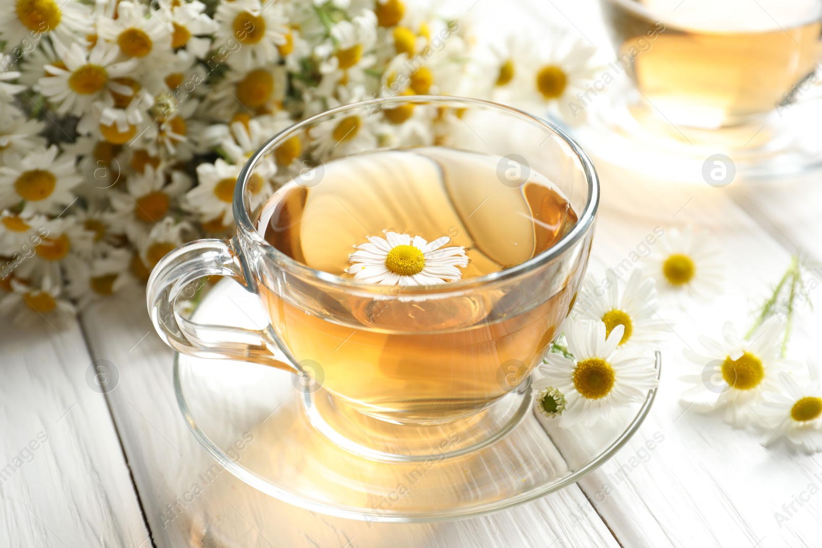Aromatic tea in glass cup and chamomile flowers on white wooden table, closeup Photo of Aromatic tea in glass cup and chamomile flowers on white wooden table, closeup