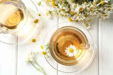 Photo of Aromatic tea in glass cup and chamomile flowers on white wooden table, flat lay