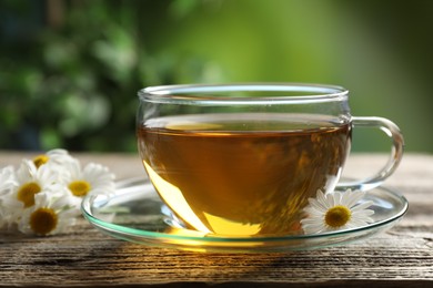 Photo of Aromatic tea in glass cup and chamomile flowers on wooden table, closeup