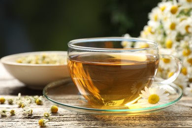 Photo of Aromatic tea in glass cup and chamomile flowers on wooden table, closeup