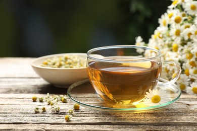 Photo of Aromatic tea in glass cup and chamomile flowers on wooden table, closeup