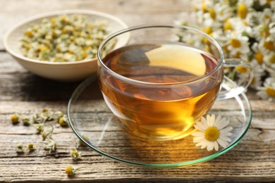 Photo of Aromatic tea in glass cup and chamomile flowers on wooden table, closeup