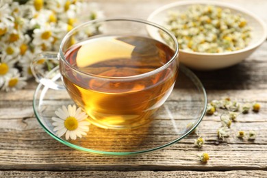 Photo of Aromatic tea in glass cup and chamomile flowers on wooden table, closeup