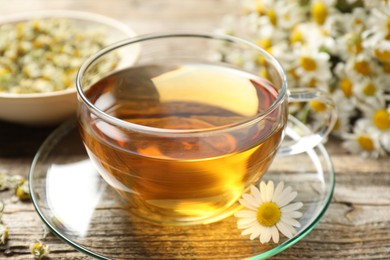Photo of Aromatic tea in glass cup and chamomile flowers on wooden table, closeup