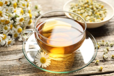 Photo of Aromatic tea in glass cup and chamomile flowers on wooden table, closeup