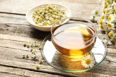 Photo of Aromatic tea in glass cup and chamomile flowers on wooden table, closeup