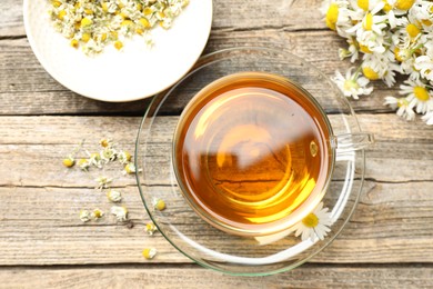 Photo of Aromatic tea in glass cup and chamomile flowers on wooden table, flat lay