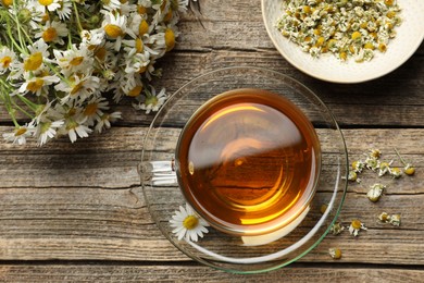 Photo of Aromatic tea in glass cup and chamomile flowers on wooden table, flat lay