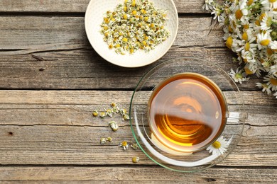 Photo of Aromatic tea in glass cup and chamomile flowers on wooden table, flat lay. Space for text