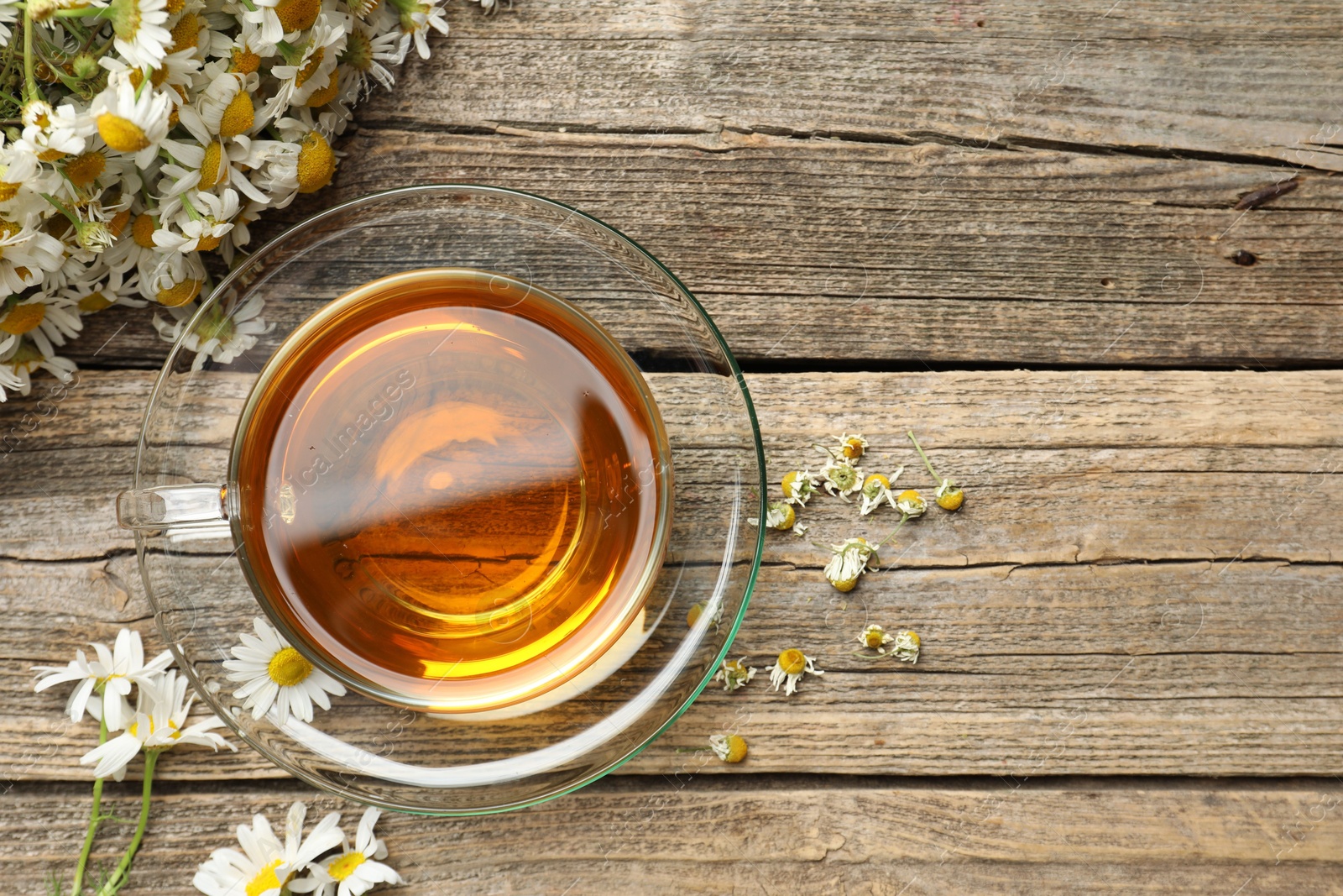 Aromatic tea in glass cup and chamomile flowers on wooden table, flat lay. Space for text Photo of Aromatic tea in glass cup and chamomile flowers on wooden table, flat lay. Space for text