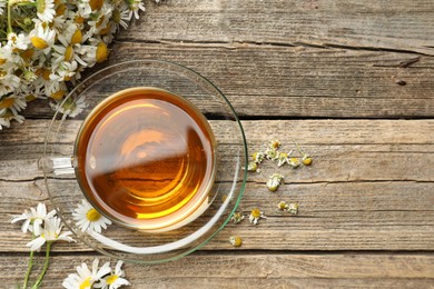Photo of Aromatic tea in glass cup and chamomile flowers on wooden table, flat lay. Space for text