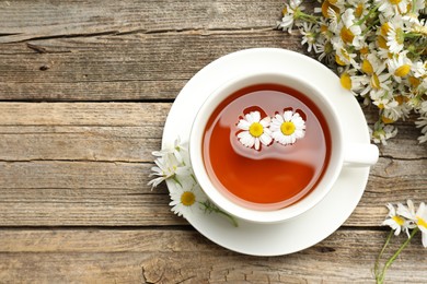 Photo of Aromatic tea in cup and chamomile flowers on wooden table, flat lay. Space for text