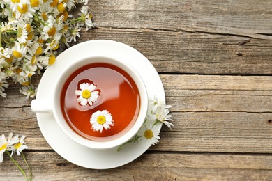 Photo of Aromatic tea in cup and chamomile flowers on wooden table, flat lay. Space for text