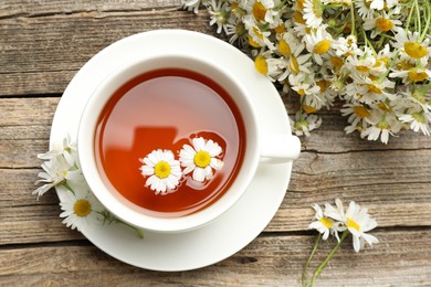 Photo of Aromatic tea in cup and chamomile flowers on wooden table, flat lay