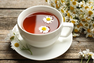 Photo of Aromatic tea in cup and chamomile flowers on wooden table, closeup