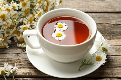 Photo of Aromatic tea in cup and chamomile flowers on wooden table, closeup