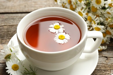 Photo of Aromatic tea in cup and chamomile flowers on table, closeup